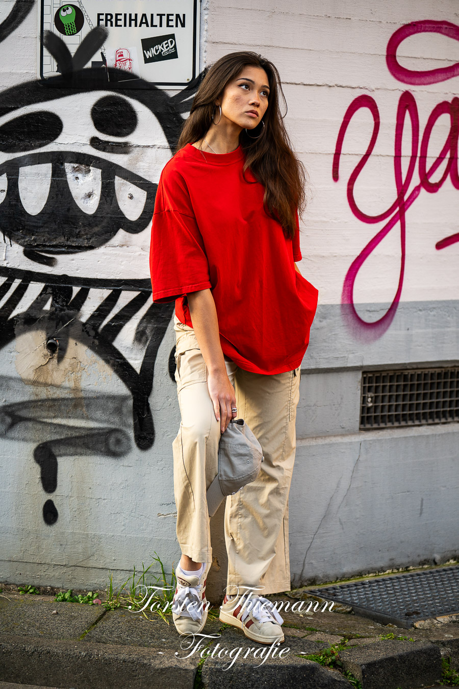 Modeaufnahmen einer jungen, asiatisch wirkenden Frau mit rotem Shirt und langen dunklen Haaren, vor einer Wand mit Graffiti.