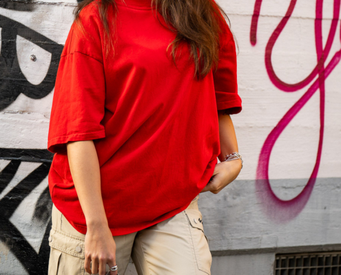 Modeaufnahmen einer jungen, asiatisch wirkenden Frau mit rotem Shirt und langen dunklen Haaren, vor einer Wand mit Graffiti.