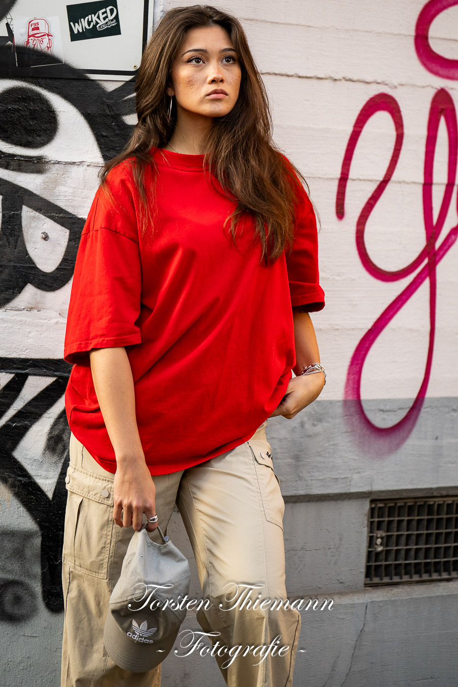 Modeaufnahmen einer jungen, asiatisch wirkenden Frau mit rotem Shirt und langen dunklen Haaren, vor einer Wand mit Graffiti.