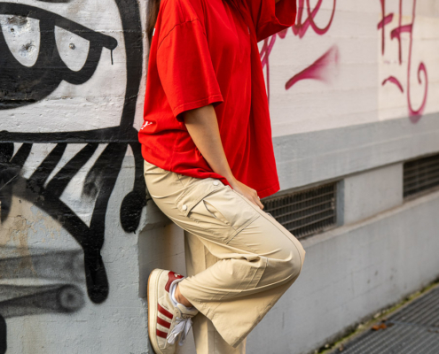 Modeaufnahmen einer jungen, asiatisch wirkenden Frau mit rotem Shirt und langen dunklen Haaren, vor einer Wand mit Graffiti.