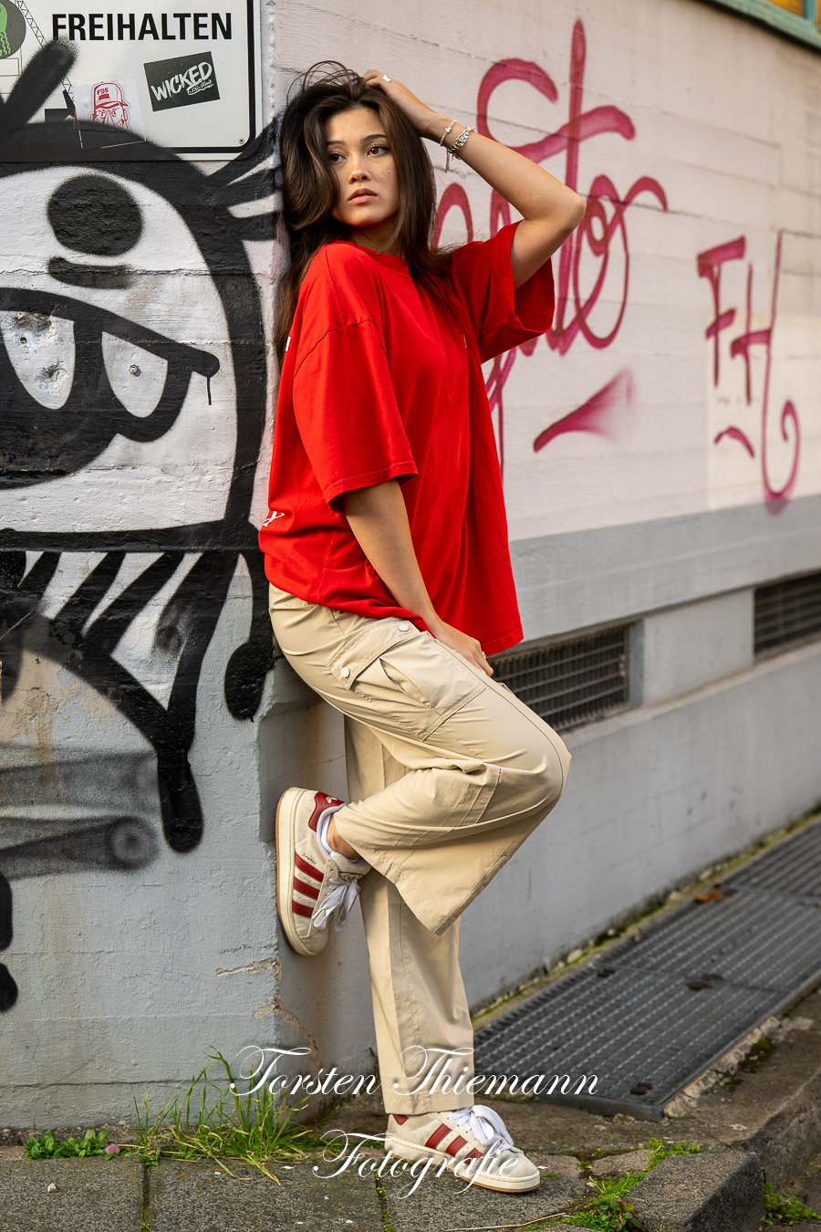 Modeaufnahmen einer jungen, asiatisch wirkenden Frau mit rotem Shirt und langen dunklen Haaren, vor einer Wand mit Graffiti.