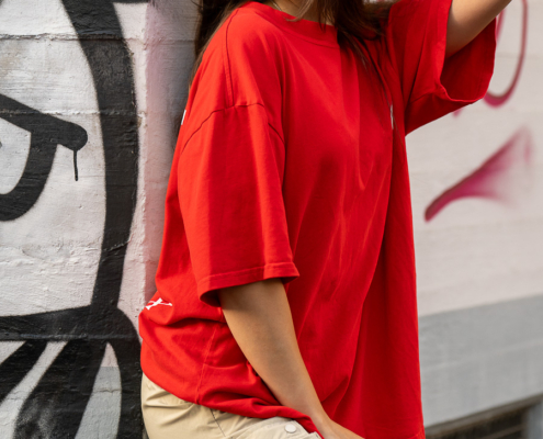 Modeaufnahmen einer jungen, asiatisch wirkenden Frau mit rotem Shirt und langen dunklen Haaren, vor einer Wand mit Graffiti.