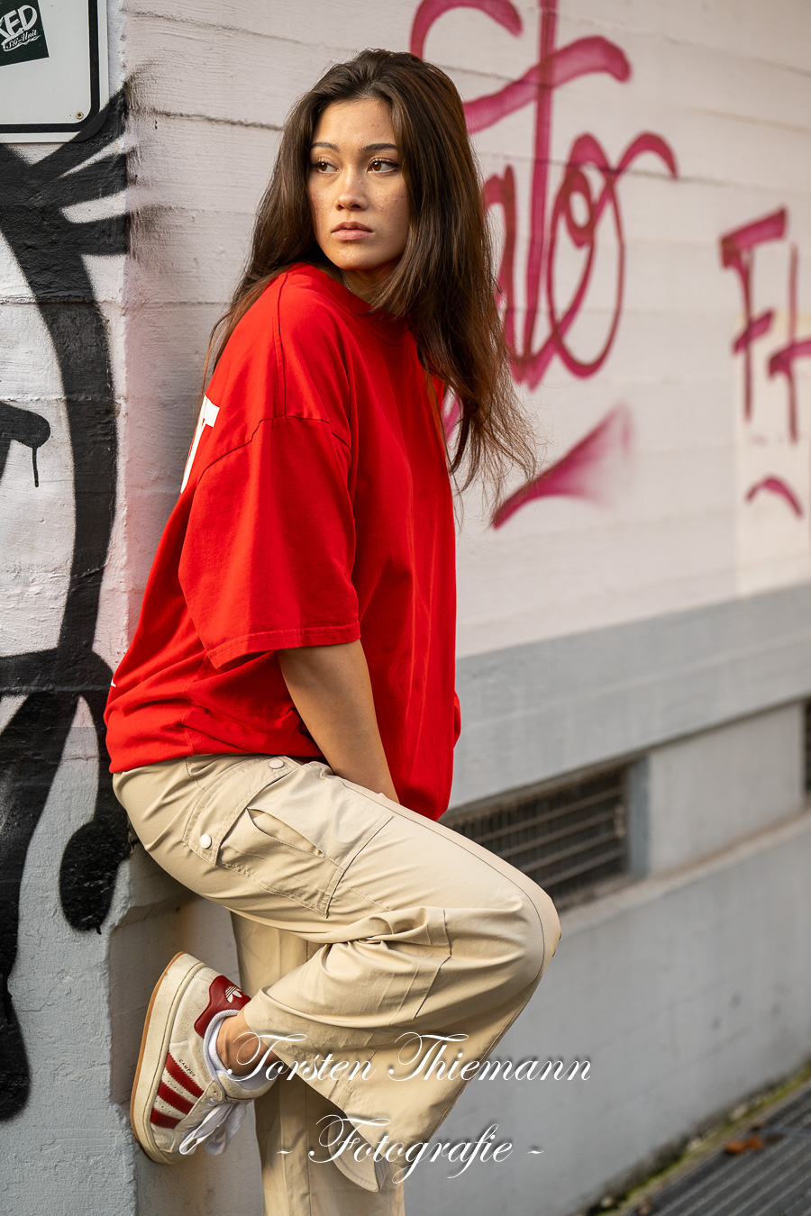 Modeaufnahmen einer jungen, asiatisch wirkenden Frau mit rotem Shirt und langen dunklen Haaren, vor einer Wand mit Graffiti.