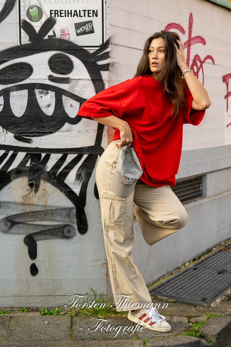 Modeaufnahmen einer jungen, asiatisch wirkenden Frau mit rotem Shirt und langen dunklen Haaren, vor einer Wand mit Graffiti.